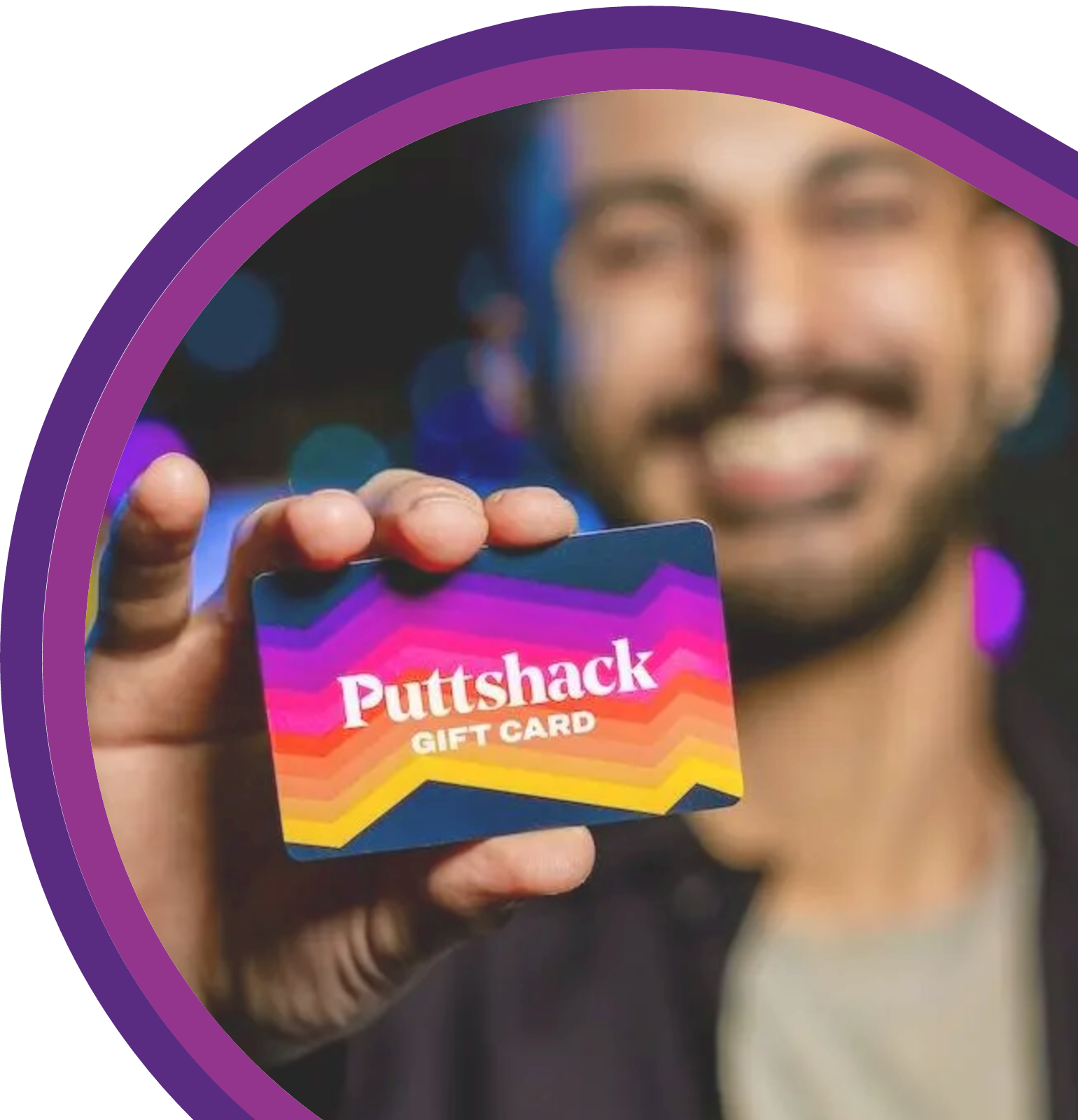 Person holding a Puttshack gift card toward the camera with an entertainment venue background