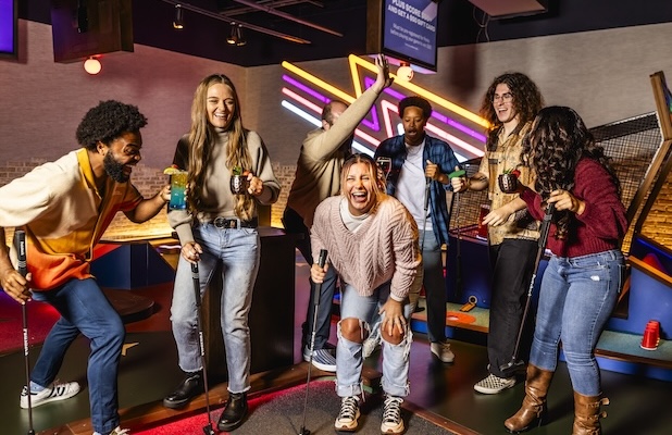 Group holding mini golf putters and drinks together on an indoor mini golf course during a group event