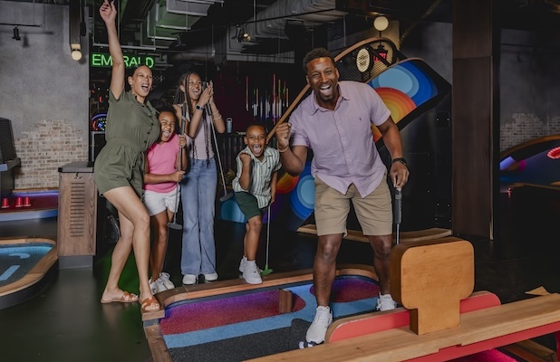Group playing indoor mini golf together on a colorful course inside an entertainment venue